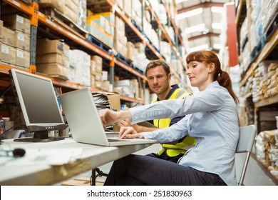 Warehouse worker and manager looking at laptop in a large warehouse