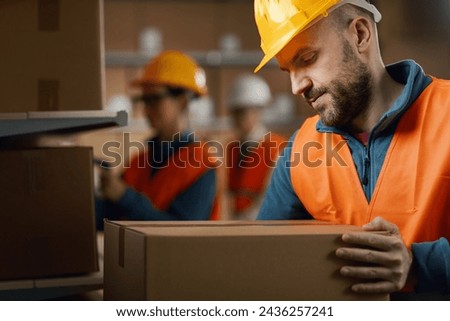 Warehouse worker moving delivery boxes, his collegues are working in the background