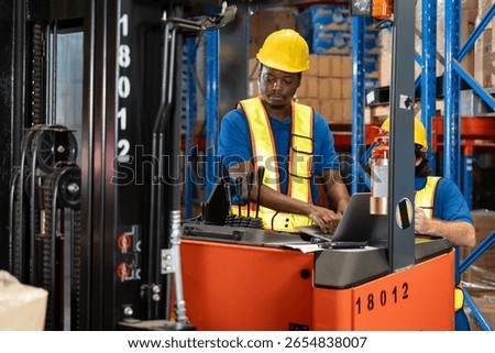 Warehouse worker operating forklift while using laptop to check inventory data. Industrial logistics and warehouse management system in action. Modern technology in supply chain operations.