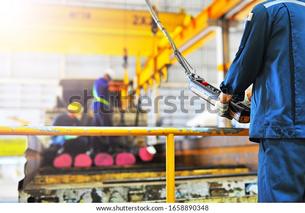 Warehouse worker\
push remote control switch for electric crane hook to loading round\
steel bars into the\
truck.