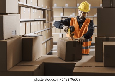 Warehouse worker sealing a cardboard box with adhesive tape, logistics and shipment concept - Powered by Shutterstock