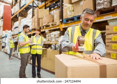 Warehouse Worker Sealing Cardboard Boxes For Shipping In A Large Warehouse