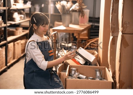 Warehouse worker sorting metal cup in storage room with cardboard box and warm light