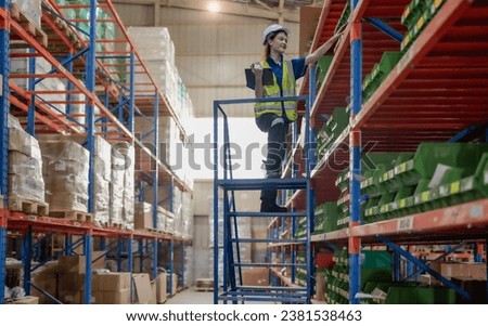 Warehouse worker standing on ladder checking stock on shelf. Female blue collar staff in safety uniform standing on staircase working with merchandise on storage rack in store. Delivering service job.