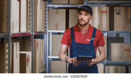 Warehouse Worker Uses Digital Tablet For Checking Stock, On the Shelves Standing Cardboard Boxes. - Powered by Shutterstock