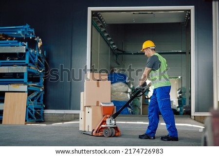 Warehouse worker using pallet jack pushing packages at storage compartment.