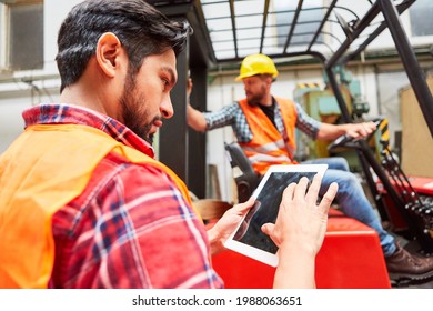 Warehouse worker using tablet computer online in factory with forklift truck in background
