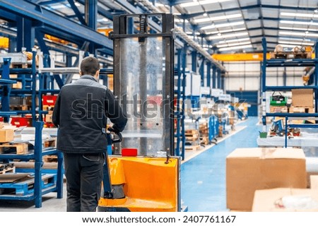Warehouse worker walking among shelves with handcart in a logistic factory