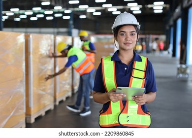 Warehouse Worker Woman With Hardhats And Reflective Jackets Using Tablet, Walkie Talkie Radio While Looking At Camera Controlling Stock And Inventory In Retail Warehouse Logistics, Distribution Center