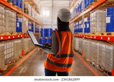 Warehouse worker woman. Storage of fuels and lubricants. Shelving with tanks for storage of petroleum products. Woman storekeeper with laptop. Oil warehouse supervisor back to camera