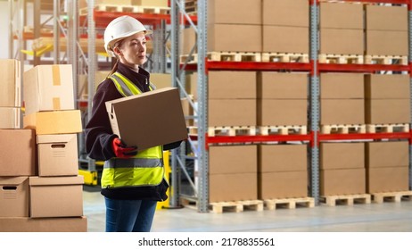 Warehouse worker. Woman works in warehouse. Girl with box. Girl in uniform of warehouse worker. Storekeeper in reflective vest. Selective focus. Storage logistics. Woman in white helmet - Shutterstock ID 2178835561