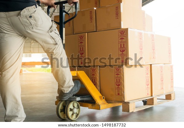 warehouse worker working with hand pallet
truck, stack cardboard boxes on wooden pallet,  cargo shipment and
transportation.