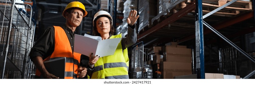 warehouse workers banner, woman with folder showing direction to middle aged colleague - Powered by Shutterstock