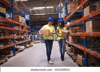 Warehouse Workers Carrying Boxes In Storage Area Putting Them On Shelves. Teamwork In Distribution Center.