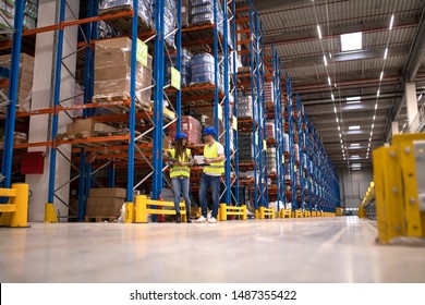 Warehouse Workers Discussing About Logistics And Distribution Packages To The Market. Teamwork In Warehouse Storage Center.