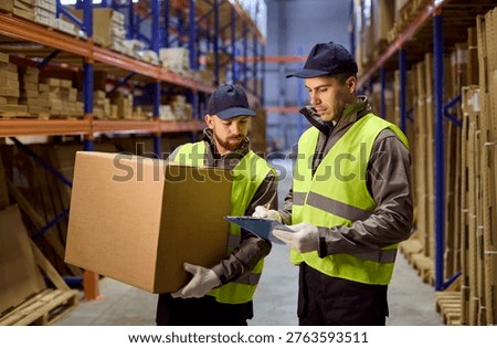 Warehouse workers inventory package with teamwork. Two loader workers check stock on clipboard in a storage warehouse for logistics delivery and shipping. Clear concept of inventory control.