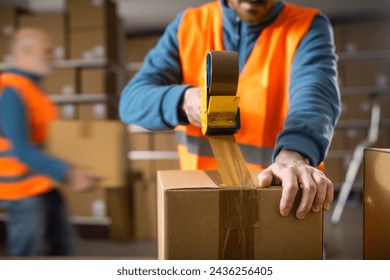 Warehouse workers preparing delivery boxes for shipping, an employee is sealing a box using a tape dispenser gun
