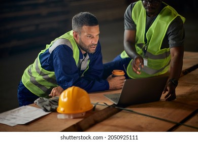 Warehouse Workers Reading Delivery Plans On Laptop While Working At Lumber Storage Compartment. 