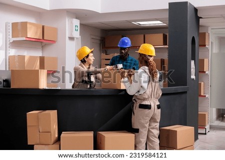 Warehouse workers team closing cardboard box with sticky tape dispenser at post office storage reception desk. Delivery service managers packing parcel with adhesive together