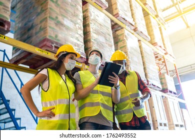 Warehouse Workers Team Meeting Inspect The Product Using A Tablet. With Wearing Face Mask And Protective Safety Helmets Standing In Storage Factory.standard To Prevent Coronavirus COVID-19 Infection