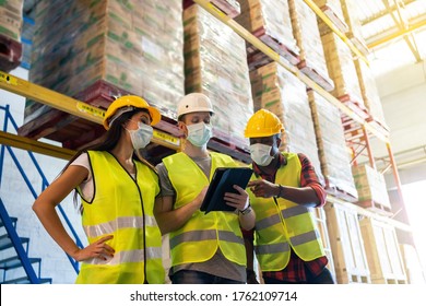 Warehouse Workers Team Meeting Using Tablet Computer With Wearing Face Mask And Protective Safety Helmet Standing In Storage Factory.standard To Prevent Coronavirus COVID-19 Infection