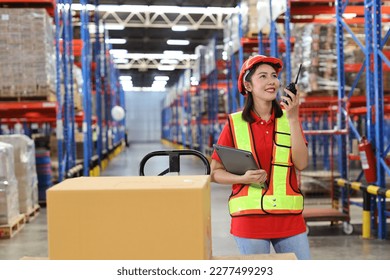 Warehouse workers woman with hardhats and reflective jackets using computer, walkie talkie radio and cardboard while controlling stock and inventory in retail warehouse logistics, distribution center - Powered by Shutterstock