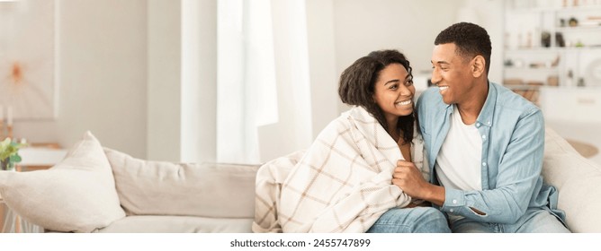 Warm and affectionate African American couple on a couch under a blanket, ideal for web-banner with copy space - Powered by Shutterstock