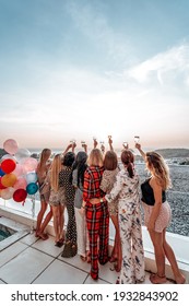 Warm and atmospheric portrait of a eight women rising their hands up holding glasses with champagne.