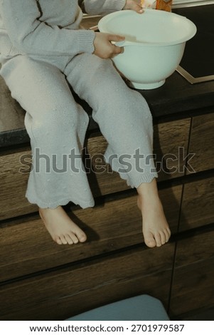 Warm and authentic maternity kitchen scene featuring a pregnant woman and her toddler daughter preparing a cake. Showing little girl’s flour-covered hands touching her mother’s baby bump.