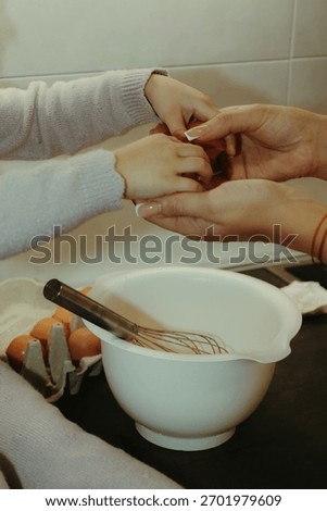 Warm and authentic maternity kitchen scene featuring a pregnant woman and her toddler daughter preparing a cake. Showing little girl’s flour-covered hands touching her mother’s baby bump.