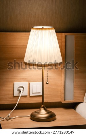 Warm bedside table lamp glowing at night in cozy bedroom, soft ambient lighting, home interior with electric lamp and wall socket.