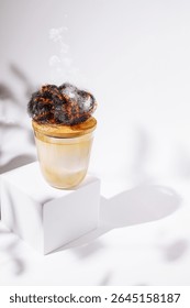 A warm beverage is elegantly presented in a transparent cup. The drink features an artistic foam design rising above, creating an inviting and cozy atmosphere.