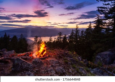 Warm Camp Fire on top of a mountain with Beautiful Canadian Nature Landscape in background during a colorful Sunset. Taken on Bowen Island, near Vancouver, British Columbia, Canada.