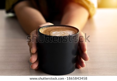 Warm coffee in a black mug with woman hand.