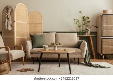Warm composition of living room interior with beige sofa, wooden coffee table, rattan sideboard, partition wall, lamp, beige carpet, stylish armchair and personal accessories. Home decor. Template.