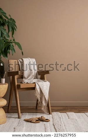 Warm and cozy composition of living room interior with copy space, stylish rattan chair, beige rug, leather slippers, plant and personal accessories. Home decor. Template.