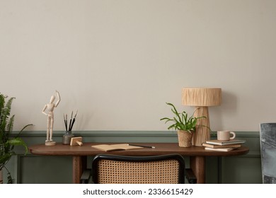 Warm and cozy composition of  workspace interior with wooden desk, rattan armchair, plant in flowerpots, books, cup, beige and green wall with stucco and personal accessories. Home decor. Template.