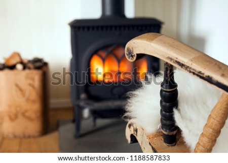 Warm and cozy corner in Scandinavian country house: wood burning stove, box of firewood and old restored rocking chair. Shallow focus on armrest. 