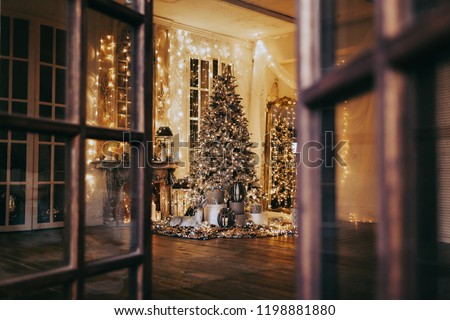 warm cozy evening in Christmas room interior design,Xmas tree decorated lights gifts, deer,candles, lanterns, garland lighting indoors fireplace.holiday.magic New year.open door to fairy tale 