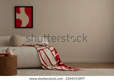 Warm and cozy living room interior with red mock up poster frame, copy space, stylish beige sofa, patterned pillow, coffee table and personal accessories. Home decor. Template.