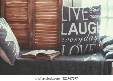 Warm And Cozy Window Seat With Cushions And A Opened Book, Light Through Vintage Shutters, Rustic Style Home Decor.