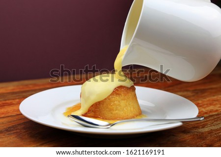 Warm Custard Being Poured From A Jug Over A Treacle Sponge Pudding.