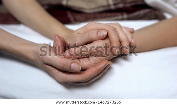 Warm daughters hands holding and calming down\
sick mother in bed,\
assistance
