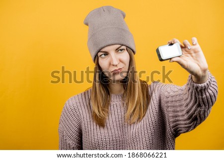 warm dressed young woman making online video streaming over yellow background. blogger and vlogger concept. copy space.
