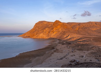 Warm evening light illuminating the dramatic cliffs and tranquil shoreline of Detwah Lagoon on Socotra Island, Yemen.