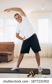 Warm Up First Cheerful Senior Man Stretching His Arms, Smiling And Looking At Camera. Morning Workout On Yoga Mat. Strong Man Doing Tilts Of The Body To The Side At Home.