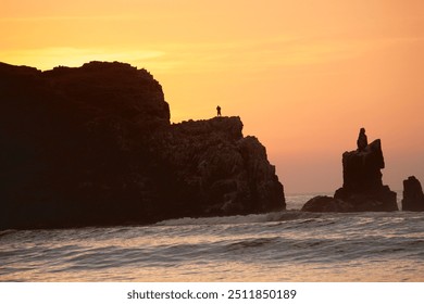 In the warm glow of a sunset, a lone silhouette stands on a cliff, facing the horizon, capturing a moment of solitude and contemplation. - Powered by Shutterstock