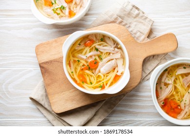 Warm healthy homemade chicken soup in white ceramic bowls on cutting board, white wooden table background. Traditional tasty chicken soup great for health and immune system. Top view - Powered by Shutterstock