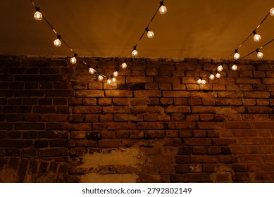 Warm incandescent string bulbs drape across a textured exposed brick wall under a muted ceiling. The glowing round bulbs cast soft amber light and subtle
