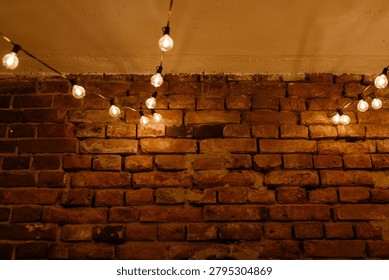 Warm incandescent string lights draped along a ceiling cast a soft amber glow over a textured exposed brick wall. The scene shows weathered red-brown bricks